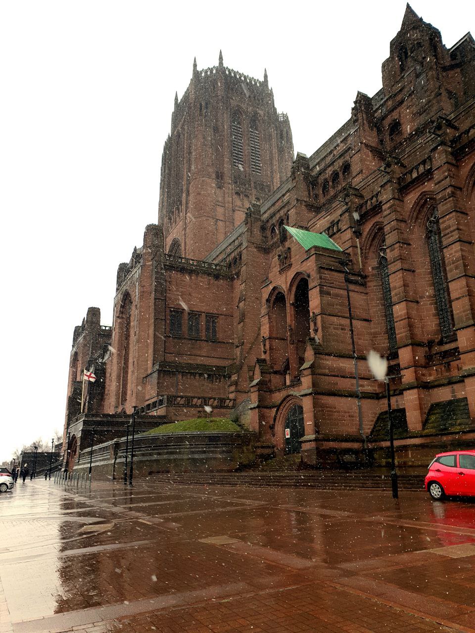 a large stone building with a flag on top with Liverpool Cathedral in the background
